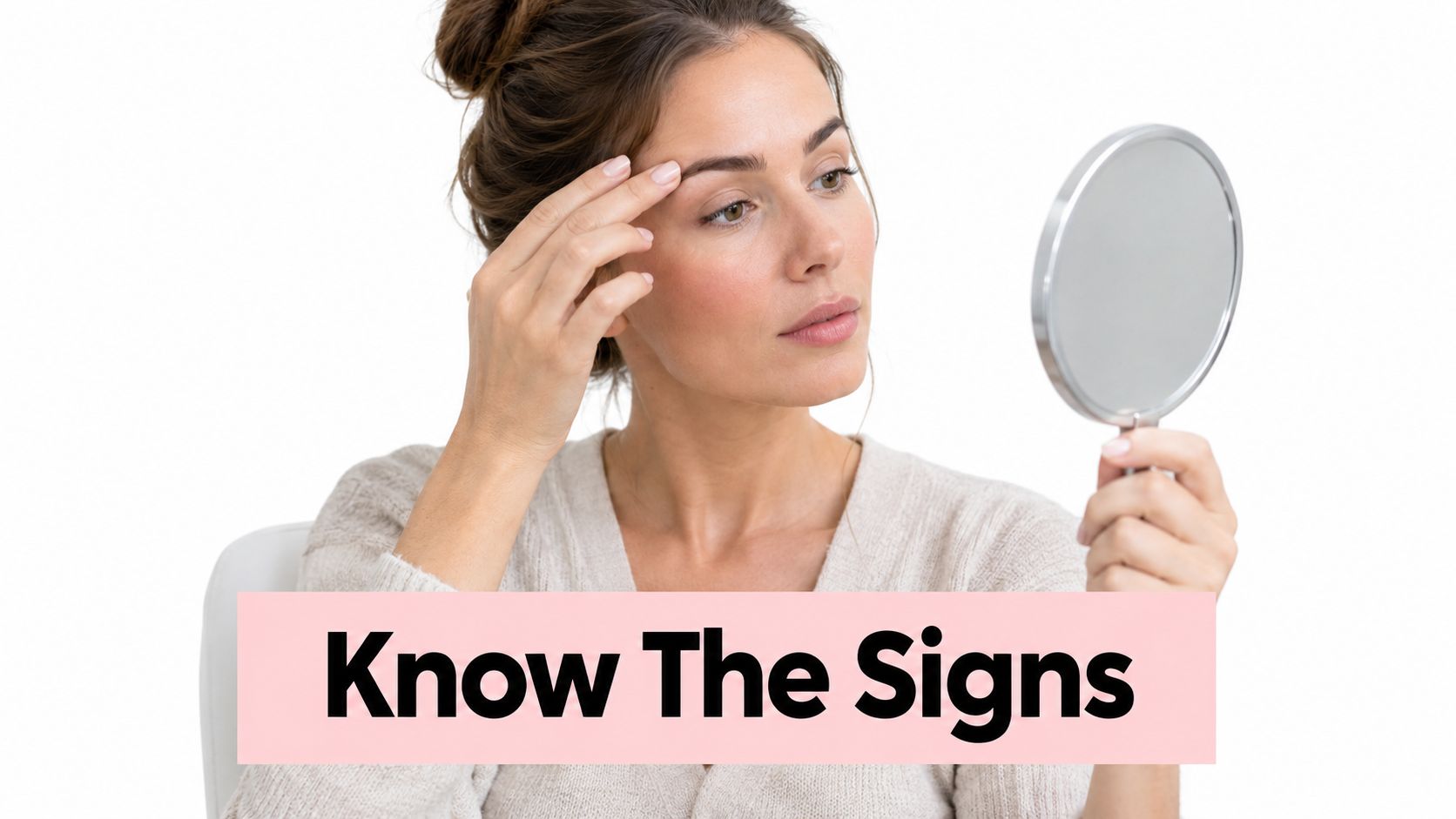 A woman looks at her eyebrows in a handheld mirror while examining signs of skin sensitivity.